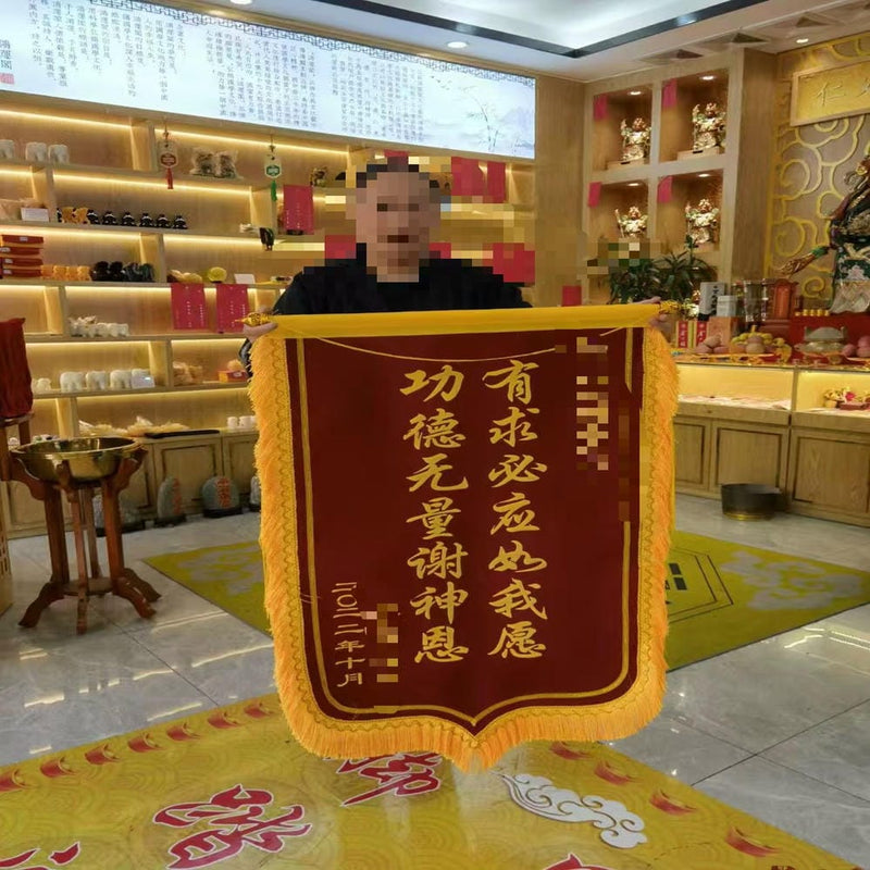 A person holding a maroon and gold banner of gratitude for answered prayers inside a ritual hall.