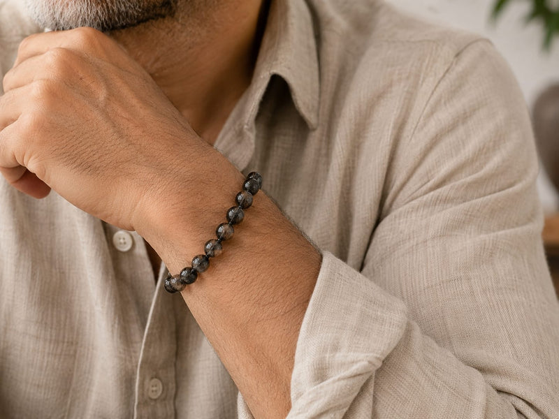 Close-up of a man wearing a Natural Black Rutilated Quartz Bracelet on his wrist, highlighting the smoky dark beads with black inclusions in an elegant everyday styling scene.