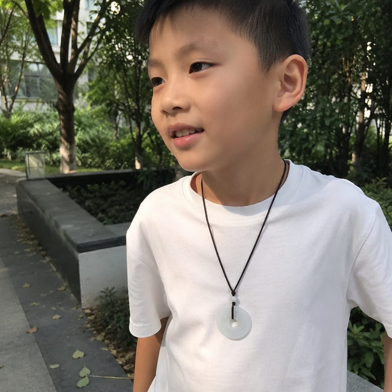Young boy wearing a white Hetian jade Peace Buckle Pendant on a black cord, styled as a daily reminder of protection, peace, and parental love.