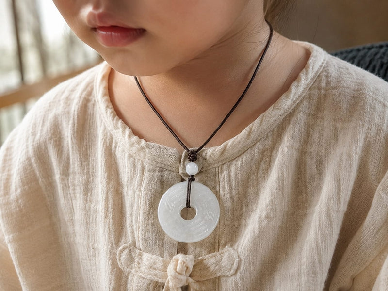 Young child wearing a white Hetian jade Peace Buckle Pendant on a black cord, symbolizing peace, care, and protection for loved ones.