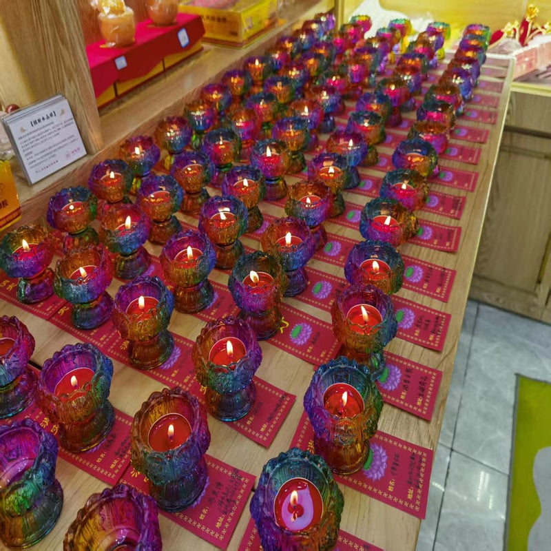 Rows of colorful votive candles on a wooden table, each placed on red paper, representing offerings and spiritual practice.