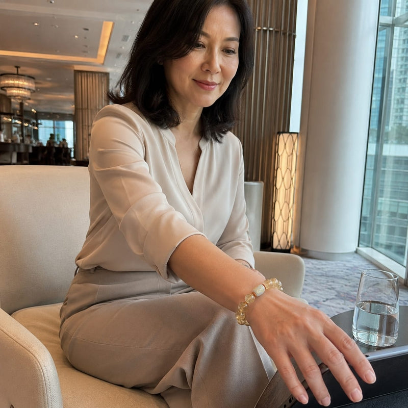 Woman seated in a modern lounge, wearing the Golden Rutilated Quartz Bracelet, subtly highlighting sophistication and refined style in a natural, candid moment.