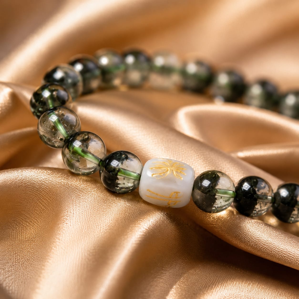 Close-up view of the Green Phantom Quartz Bracelet showing the San He Wood formation bead and reflective green phantom inclusions on a golden satin fabric.