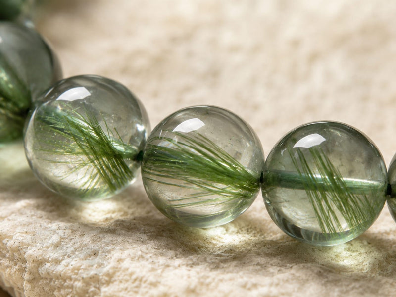 Close-up of green rutilated quartz beads with natural needle-like inclusions, highlighting the bracelet’s clear green tones and polished texture.