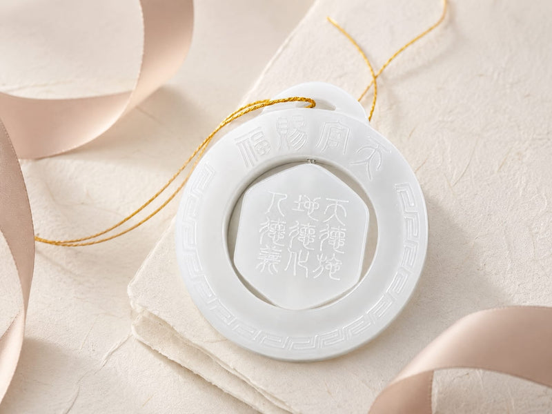 The Heavenly Blessing Talisman Pendant in white jade placed on a light-colored fabric with soft ribbons around, emphasizing its serene and intentional presentation.