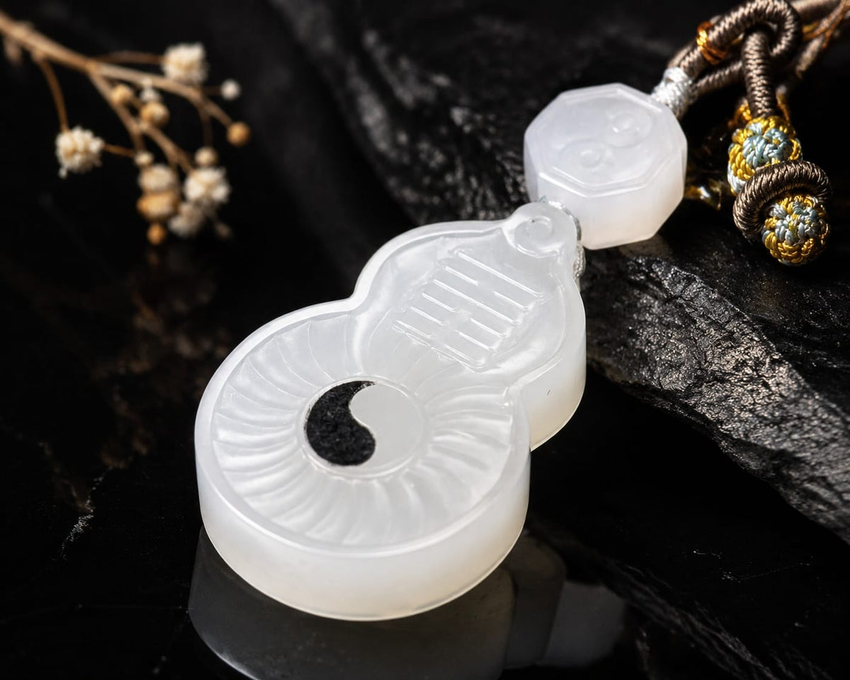 A high-quality white jade pendant shaped like a gourd, featuring a Taiji Yin-Yang symbol and Bagua trigrams, presented on a dark textured stone background with a traditional braided cord.