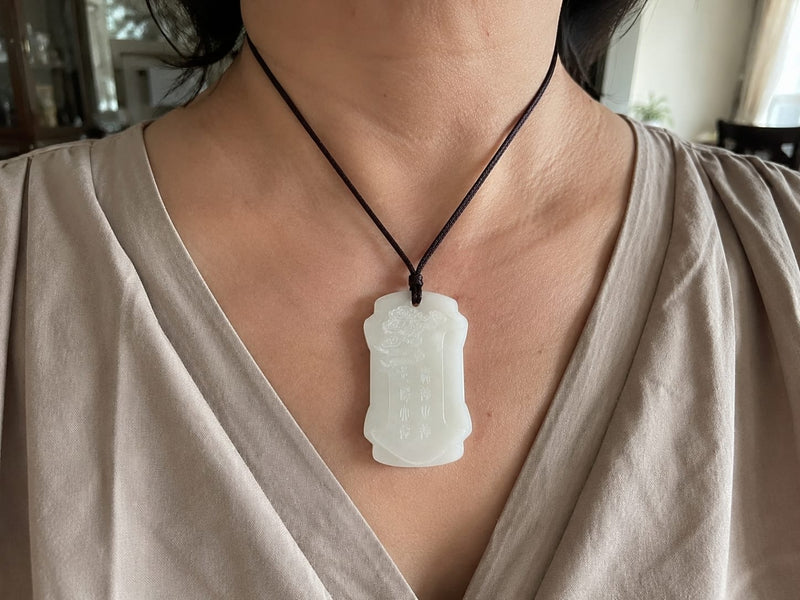 A close-up of a woman wearing the Moon Virtue jade pendant on a black cord around her neck. The pendant rests naturally on her chest, showing the smooth jade surface and carved details. The image evokes calm, centered energy and mindful daily use.