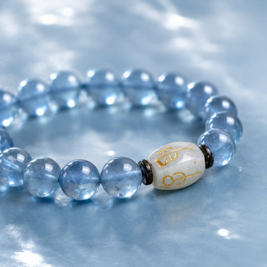 Close-up view of a Natural Aquamarine Bracelet with a “San He Water” Hetian jade charm, highlighting the translucent blue beads and gold inscriptions on a soft blue fabric.