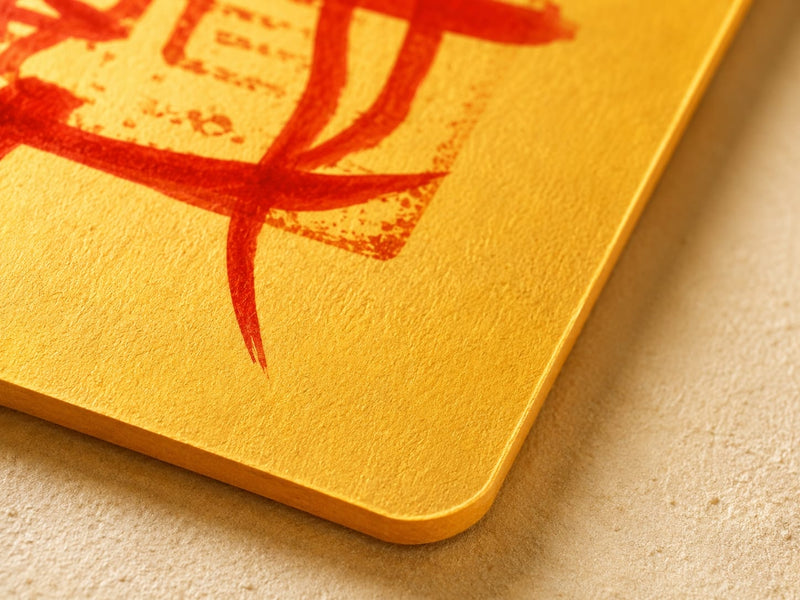 Close-up of the rounded corner and textured golden paper of a Protection & Peace Talisman, highlighting its warm color, paper grain, and refined handmade finish.