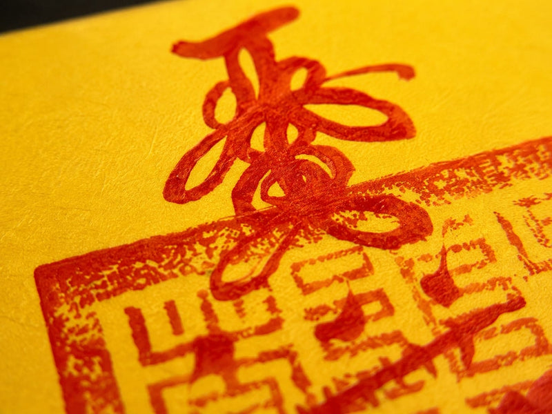 Close-up of a yellow hand-drawn Wealth Talisman inspired by the Sanqing Ling tradition, showing red ink brush strokes over a traditional Taoist seal block. Highlights the natural flow, pressure, and texture of each hand-drawn line, emphasizing its unique and sacred character.