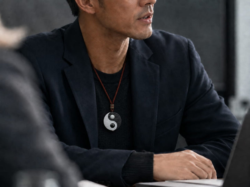 A man wearing a Taiji Yin Yang pendant in a modern meeting setting, styled with a dark blazer and black shirt to convey focus, calm confidence, and career alignment.
