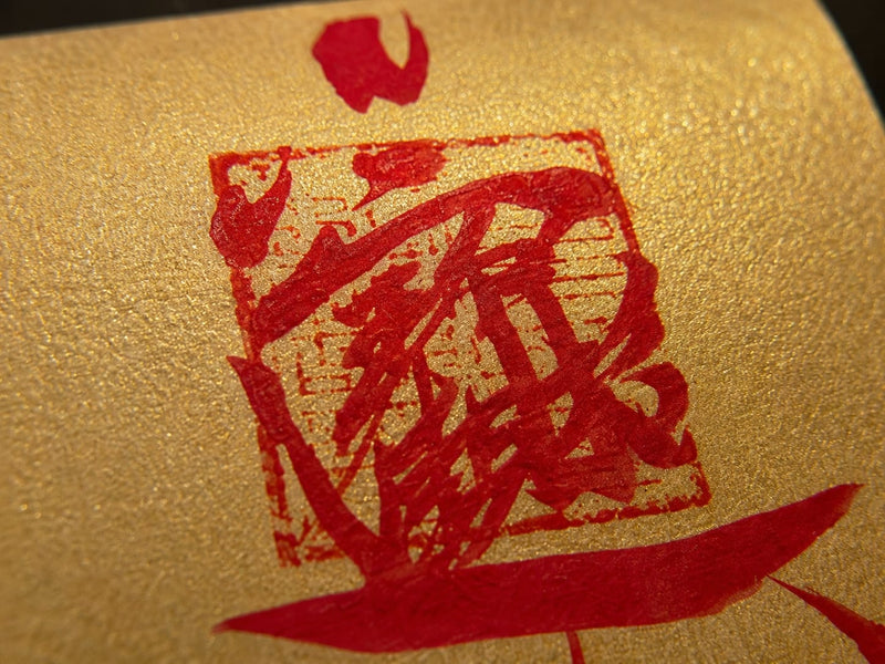 Close-up of the handcrafted red symbols on a golden Wealth Protection Talisman, showing ink texture, ritual-inspired markings, and handmade detail.