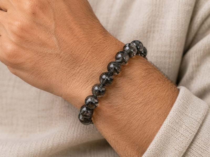 A middle-aged man wearing a Natural Black Rutilated Quartz Bracelet on his wrist, showing a close-up of the bracelet’s smoky beads with black needle-like inclusions, suggesting mindful daily wear and intention.