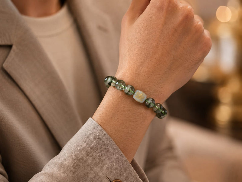 A wrist wearing a Green Phantom Quartz Bracelet with the San He Wood formation bead, styled in an elegant, everyday outfit to signify resilience, focus, and financial growth.