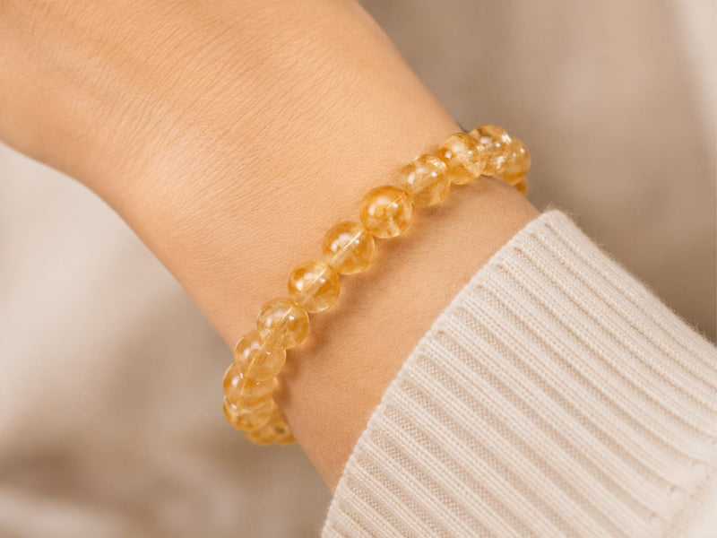 Woman’s wrist wearing the natural citrine bracelet over a cream ribbed sleeve, illustrating daily mindful wear and subtle elegance.