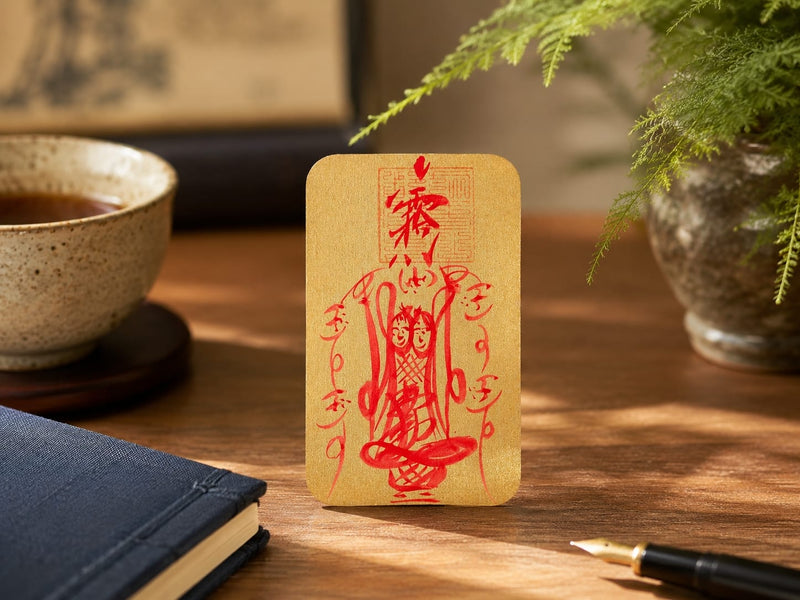 The Wenchang Talisman standing on a desk beside a cup of tea, a notebook, and plants, symbolizing mental clarity and focus. The gold card with red calligraphy is prominently displayed, enhancing a calm and thoughtful workspace.