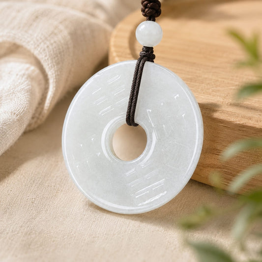 Close-up of a white Hetian jade Peace Buckle Pendant with a dark braided cord and white bead, styled with soft linen and warm wood accents.