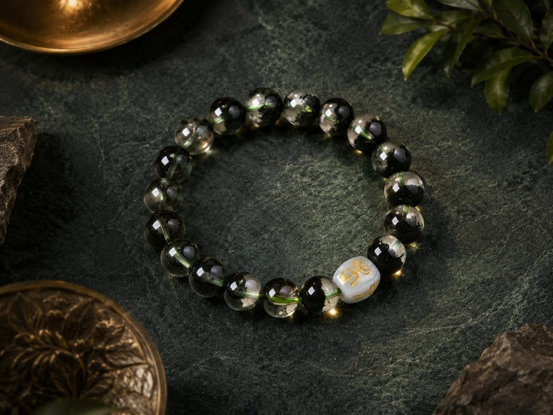 Green Phantom Quartz Bracelet displayed on a dark stone surface with decorative elements, featuring the symbolic San He Wood formation bead for courage, resilience, and long-term growth.
