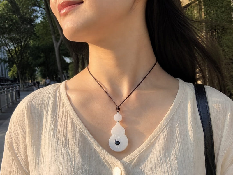 Lifestyle shot of a person wearing the Vermilion Bird white jade pendant with a black cord, outdoors in natural light, highlighting everyday elegance with a neutral top