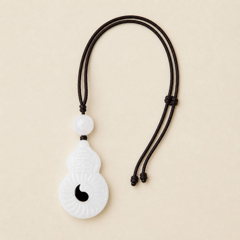 Full view of the Vermilion Bird white jade pendant with black yin detail and braided cord, laid flat on a neutral background